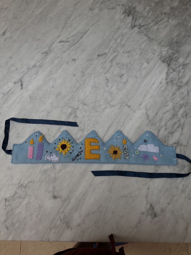 Blue felt crown laid flat showing full embroidery detail